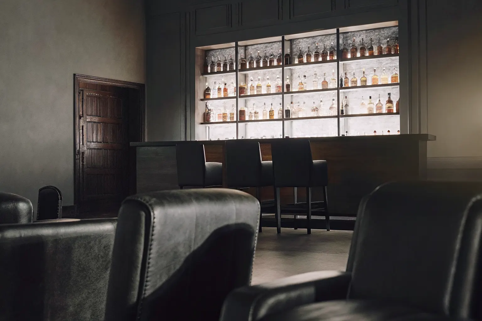 Upscale lounge and bar interior with backlit liquor shelves and warm amber lighting