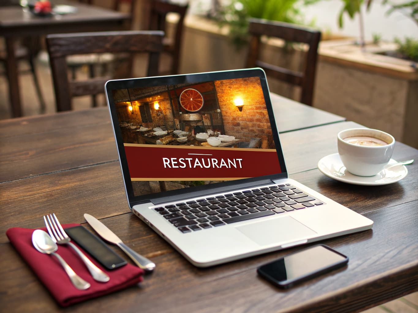 Laptop and phone showing a restaurant website on a wooden table with coffee and cutlery
