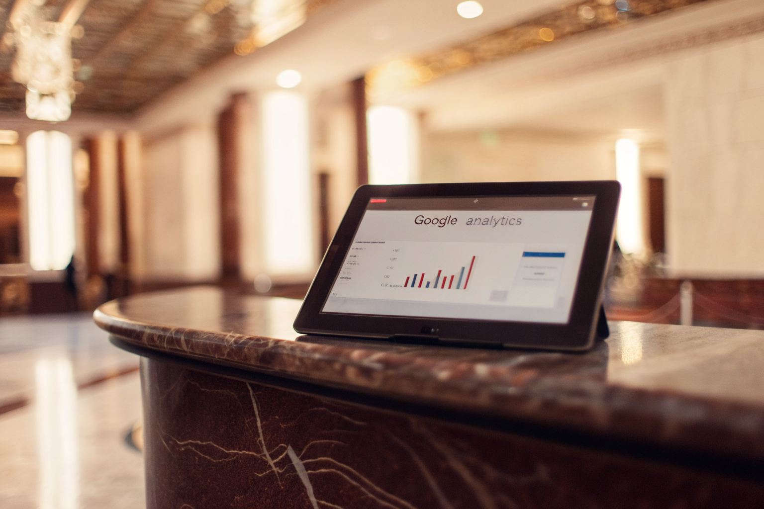Analytics dashboard on tablet at a hotel concierge desk showing mobile marketing performance metrics and booking trends
